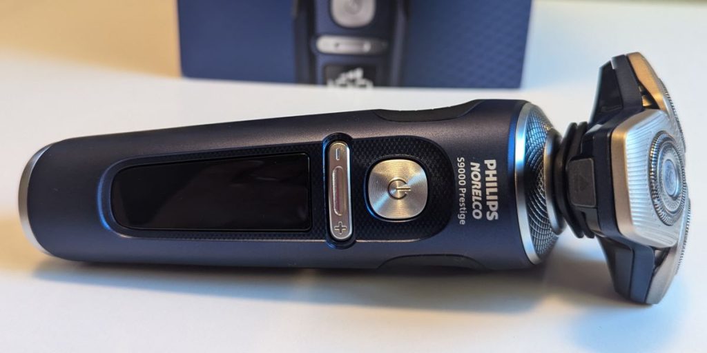 A close-up of the blue Philips Norelco S9000 Prestige Space Grade Shaver resting on its side on a white table