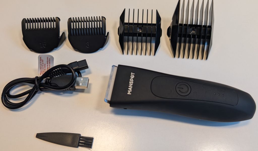 Everything in the box of the Manspot Body Hair Trimmer. The trimmer, 4 different combs, charging cord, and a small brush